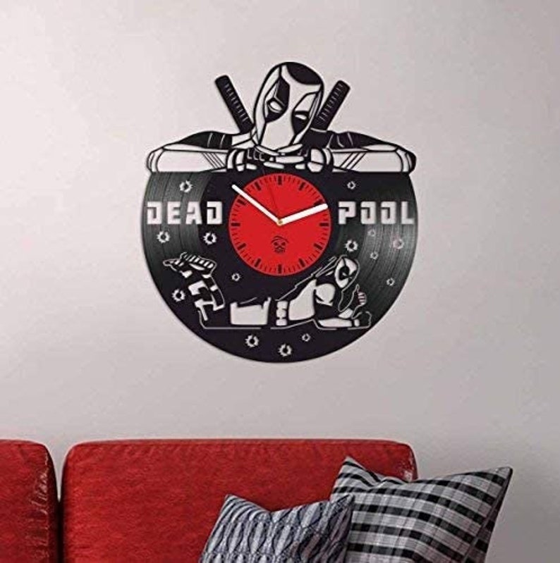 May include: A black vinyl record clock featuring a silhouette of Deadpool with the text "DEAD POOL" on the record. The clock has a red face with white hands and black numbers.