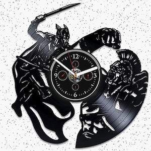 May include: Black vinyl record clock featuring a silhouette of a gladiator fighting a warrior. The clock face is black with white hands and Roman numeral markings.