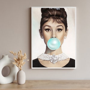 May include: A black and white portrait of a woman with a large blue bubble gum in her mouth. She is wearing a pearl necklace and a black dress. The background is a light gray.