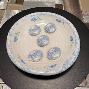 May include: A white ceramic dish with a blue and white floral pattern. The dish has four indented circles for serving individual portions.