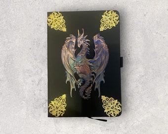 May include: A black notebook featuring a central three-dimensional dragon sculpture with iridescent blue and purple tones. The cover is decorated with four ornate gold-colored filigree corner accents, providing a contrast to the smooth black surface.
