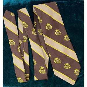 May include: A brown and tan striped tie featuring the text "BURGER QUEEN" and a crown logo. The tie is made of a smooth fabric and is displayed in a flat lay. The tie is a vintage item.