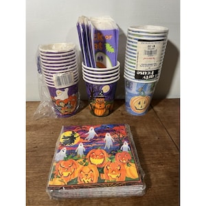 May include: A collection of Halloween-themed party supplies, including paper cups with purple and blue stripes, napkins with jack-o'-lanterns and ghosts, and cups with pumpkin and witch designs. The items are arranged on a wooden surface.