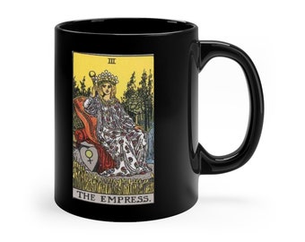May include: Black ceramic mug with a white image of the Empress tarot card. The card features a woman sitting on a throne with a crown and a scepter. The card number III is in the top left corner and the text "THE EMPRESS." is at the bottom.