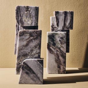 May include: A collection of gray and white marble sculptures with dark veining. The pieces are rectangular and square, with some having curved edges. The sculptures are arranged in a balanced composition against a neutral background.