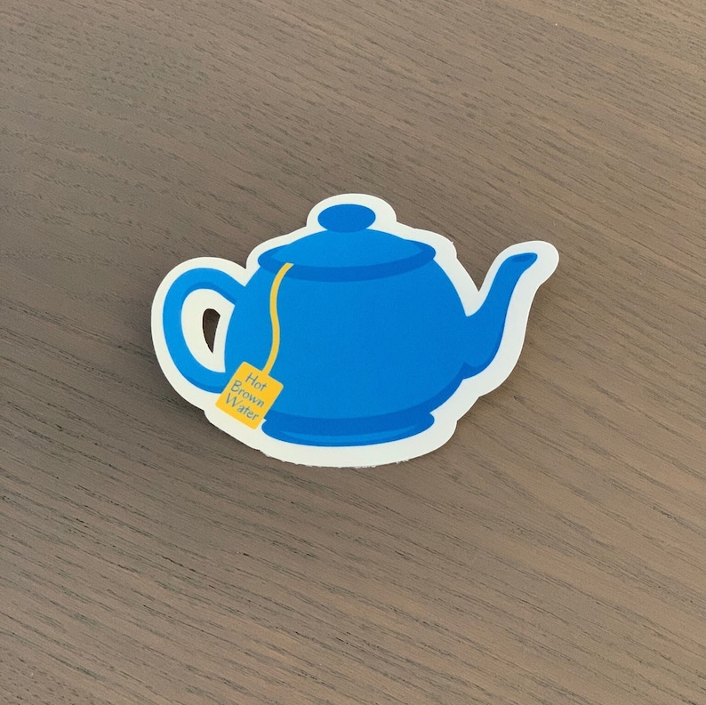 Pode incluir: Um autocolante de bule azul com uma borda branca. O bule tem uma al&ccedil;a, um bico e uma tampa. Um saquinho de ch&aacute; amarelo com as palavras "Hot Brown Water" est&aacute; preso ao bule.