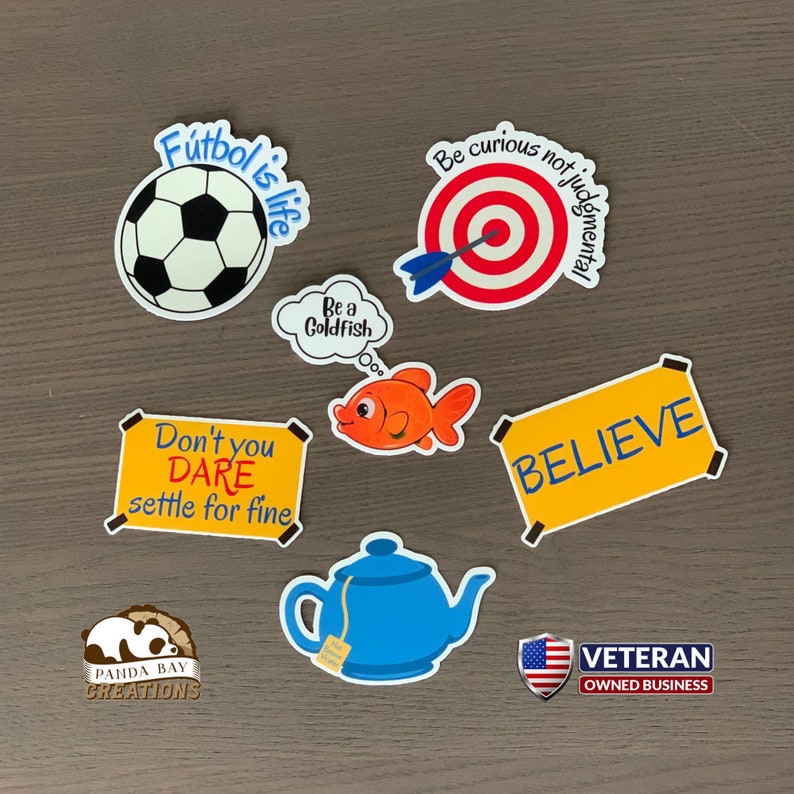 Pode incluir: Uma cole&ccedil;&atilde;o de autocolantes coloridos com v&aacute;rios desenhos e texto. Os desenhos incluem uma bola de futebol com "Futbol is life", um alvo com "Be curious not judgmental", um peixe dourado e uma chaleira. Outros autocolantes dizem "Believe" e "Don't you DARE settle for fine".