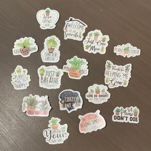 May include: A collection of 15 colorful plant-themed stickers with various sayings, including "Keep Growing", "Forever Green", "Just Breathe", "Positive Vibes", "Plants Make Me Happy", "Crazy Plant Lady", "Life is Short Buy More Plants", "Welcome to My Garden", "Just One More", "Plant Lover", "Thanks for Helping Me Grow", "Please Don't Die", "I Love So Much", "Grow Your Own Way", and "Belong Among the Wildflowers".