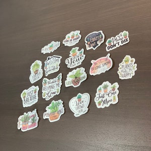 May include: A collection of 15 colorful plant-themed stickers with various sayings, including "Just Breathe", "Grow Your Own Way", "Love Grows Here", and "Plants Make Me Happy".