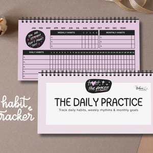 May include: Two spiral-bound habit trackers. The top one is open, showing a monthly calendar layout with the text "You are enough, don't forget that." The bottom tracker reads "The Daily Practice."