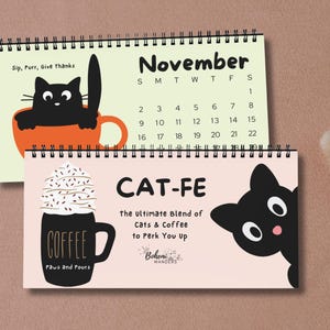Könnte beinhalten: Ein Schreibtischkalender mit einer schwarzen Katzenillustration und dem Text "Sip, Purr, Give thanks" oben. Der Kalender ist für November und zeigt eine schwarze Katzenillustration in einer Kaffeetasse. Der untere Kalender ist rosa mit einer schwarzen Katzenillustration und dem Text "CAT-FE The ultimate Blend of Cats & Coffee to Perk You Up Bohemian Wanderers".