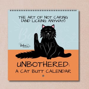 Op de afbeelding: Een spiraalgebonden kalender met een illustratie van een zwarte kat. De kat zit met zijn achterwerk naar de kijker. De kalender heeft de tekst "THE ART OF NOT CARING (AND LICKING ANYWAY)" en "UNBOTHERED: A CAT BUTT CALENDAR".