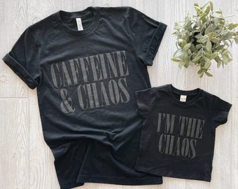 May include: Two black t-shirts with a matching design. The larger shirt says "Caffeine & Chaos" in gray text. The smaller shirt says "I'm the Chaos" in gray text.