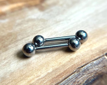 Puede incluir: Una joya corporal tipo barra industrial de tono plateado que presenta dos barras rectas paralelas conectadas por cuatro pequeñas esferas lisas en los extremos. El metal tiene un acabado pulido y reflectante, creando una estética simple.