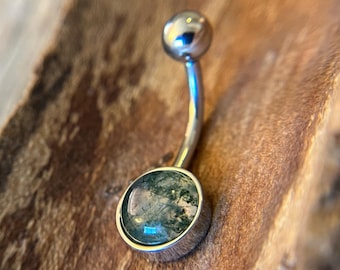 Puede incluir: Un piercing de ombligo plateado con una piedra verde y gris.
