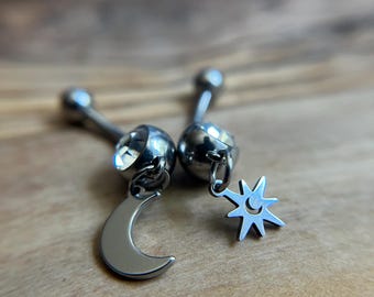 Puede incluir: Dos piercings para el ombligo de tono plateado con diseño de barra curva. Una pieza tiene un dije colgante de media luna, mientras que la otra presenta un dije en forma de estrella. Ambos incluyen una gema redonda y transparente.