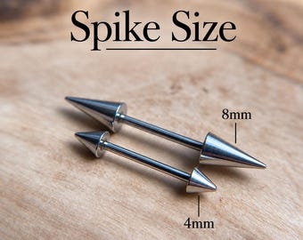 Puede incluir: Dos piercings tipo barbell de metal plateado con extremos en forma de punta. El texto Spike Size aparece sobre los objetos. Un barbell tiene puntas de 8mm, mientras que el otro tiene puntas de 4mm, según indican las etiquetas en la imagen.