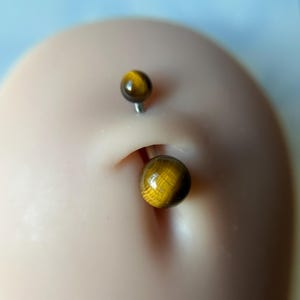 May include: A belly button piercing with two gold tiger's eye beads.