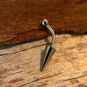 May include: A silver belly button ring with a small ball on one end and a pointed cone on the other end.