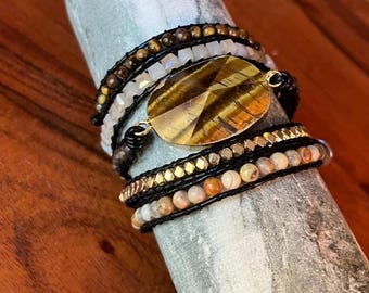 Puede incluir: Una pulsera envolvente de varias vueltas con una gran pieza central ovalada de ojo de tigre facetado, filas de cuentas de ojo de tigre marrón, cuentas cuadradas blancas, cuentas metálicas doradas facetadas y pequeñas cuentas redondas de piedra beige.