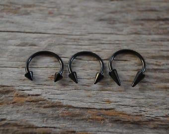 May include: Three black horseshoe-shaped rings with pointed ends. The rings are made of metal and have a black finish.