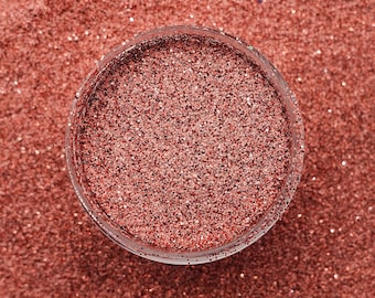 May include: A close-up view of a glass jar filled with fine rose gold glitter. The glitter is a shimmery, metallic shade of pink and gold.