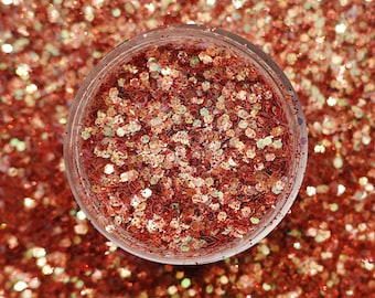 May include: A clear glass jar filled with red and gold glitter. The glitter is iridescent and has a variety of sizes.