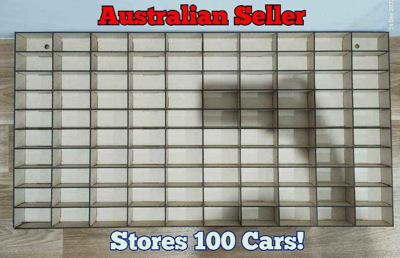 Pode incluir: Uma prateleira de armazenamento de madeira com 100 compartimentos, projetada para guardar carros de brinquedo. A prateleira &eacute; feita de madeira marrom claro e tem uma moldura preta. O texto "Stores 100 Cars!" &eacute; impresso abaixo da prateleira.