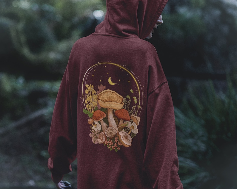 Peut inclure: Sweat-shirt bordeaux avec un motif de champignons, de fleurs et d'un croissant de lune dans un cercle au dos.