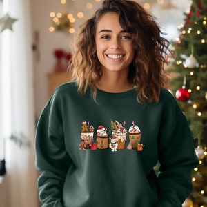 May include: Dark green sweatshirt featuring a festive graphic of holiday-themed beverages, including gingerbread lattes and hot cocoa, with candy canes and Christmas tree accents. The design is centered on the front of the sweatshirt.