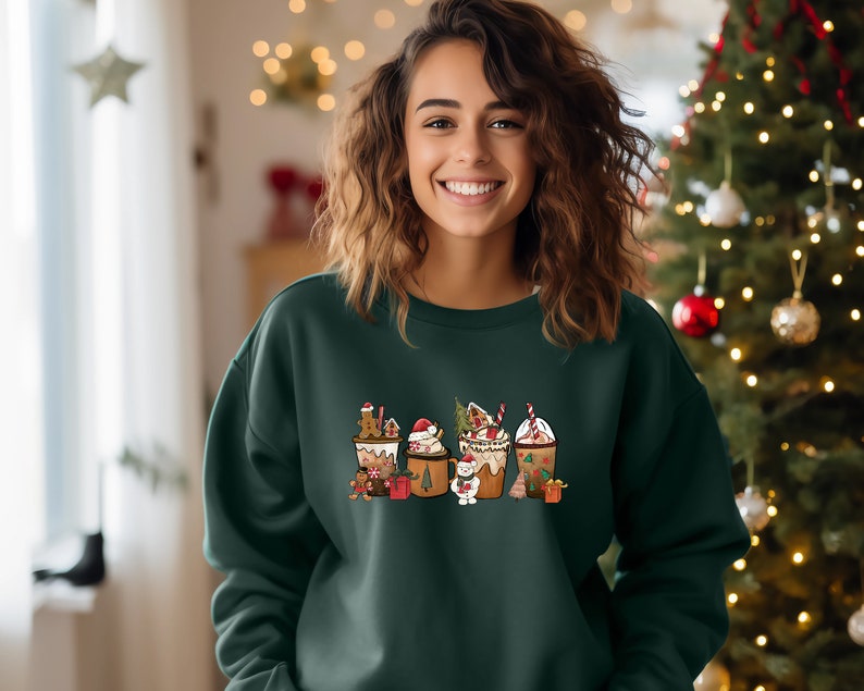 May include: Dark green sweatshirt featuring a festive graphic of holiday-themed beverages, including gingerbread lattes and hot cocoa, with candy canes and Christmas tree accents. The design is centered on the front of the sweatshirt.