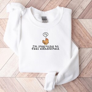 Pu&ograve; includere: Felpa bianca con un grafico di pollo pixelato e il testo "Sto iniziando a sentirmi esausto."