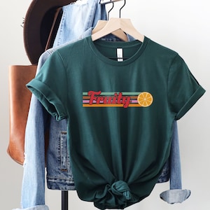 May include: A green t-shirt with a retro-style graphic that says "Fruity" with a colorful striped background and an orange slice.