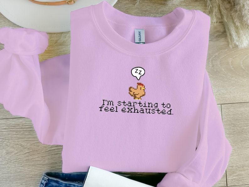 Pu&ograve; includere: Una felpa di colore lilla chiaro con un'immagine di pollo pixelata e il testo "Sto iniziando a sentirmi esausto."