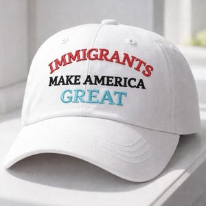 May include: White baseball cap with the embroidered text "IMMIGRANTS MAKE AMERICA GREAT" in red, black, and blue. The hat is on a white surface.