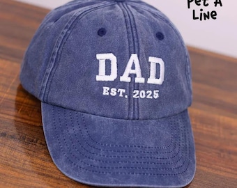 May include: A blue denim baseball cap with white embroidered text that reads "DAD EST. 2025".
