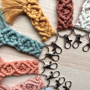 May include: A set of colorful macrame keychains with silver key rings. The keychains are made with different colored cords and have a tassel at the end.