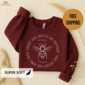 May include: A maroon sweatshirt featuring a white bee graphic and the words "Brave, Vibrant, Wild, Creative, You, Independent, Tough, Confident, Kind, Humble". The words "Super Soft" are also visible.