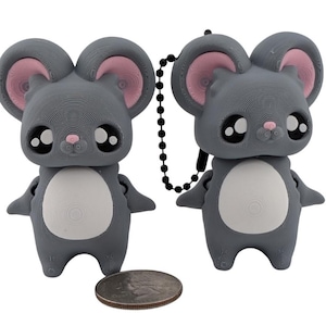 May include: Two gray mouse-shaped keychains with large black eyes, pink ears, and a white belly. The keychains are connected by a black chain. A U.S. quarter is in the foreground for size comparison.