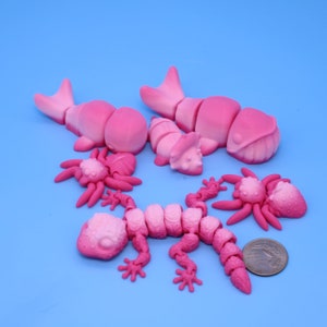 May include: Five pink plastic articulated animal toys: a whale, a lizard, a spider, a dinosaur, and another spider. The toys are on a blue background.