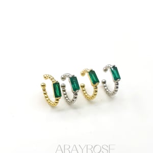 May include: Four ear cuffs with a green rectangular gemstone. Two are gold-toned, and two are silver-toned. The cuffs have a beaded design. The brand name "ARAYROSE" is at the bottom.