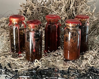 May include: Five small glass bottles with red wax seals and a dark liquid inside. The bottles are sitting on a bed of dried moss and surrounded by black metal nails.