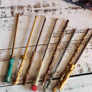 May include: A collection of eight wooden wands with different coloured tips and designs. The wands are arranged on a white wooden surface.