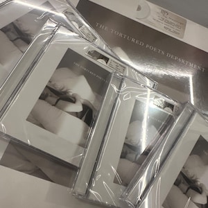 May include: Multiple copies of a CD album by The Tortured Poets Department. The album cover features a black and white photo of a person lying on a bed.