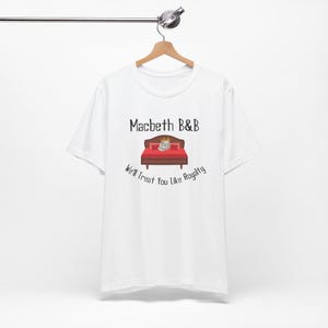 May include: White t-shirt with a black graphic of a bed with a crown and the text "Macbeth B&B We'll Treat You Like Royalty"