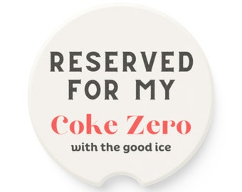 May include: White round coaster with black text that reads "Reserved for my Coke Zero with the good ice".