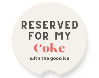 May include: Cream-colored car coaster with the text "RESERVED FOR MY Coke with the good ice" in black and red lettering. The coaster has a curved notch on one side.