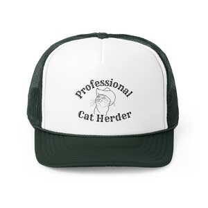May include: White and green trucker hat with a black outline of a cat wearing a cowboy hat and the text "Professional Cat Herder".