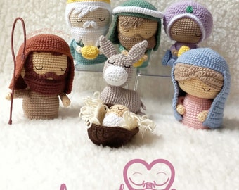 Puede incluir: Una escena de la natividad hecha a crochet con un pastor marrón, un rey mago con túnica verde, una reina maga con túnica morada, una María con túnica azul, un burro y un bebé Jesús en un pesebre.