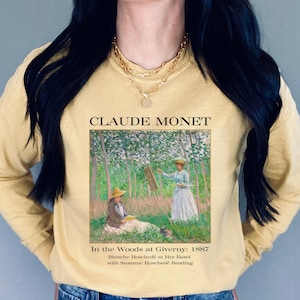 May include: A yellow long-sleeved shirt with a painting of Claude Monet's "In the Woods at Giverny: 1887" featuring Blanche Hosched&eacute; at Her Easel with Suzanne Hosched&eacute; Reading.